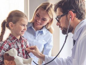 kleines Mädchen mit Mutter wird von Arzt mit Stethoskop untersucht